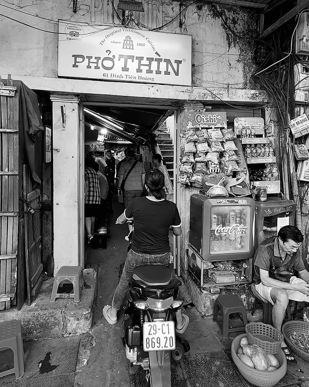 Black and white street scene outside a small shop.