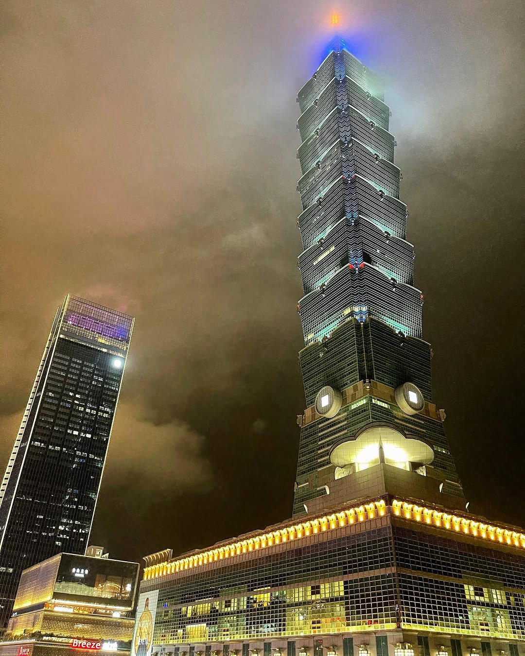 A lit tower disappearing into clouds at night.